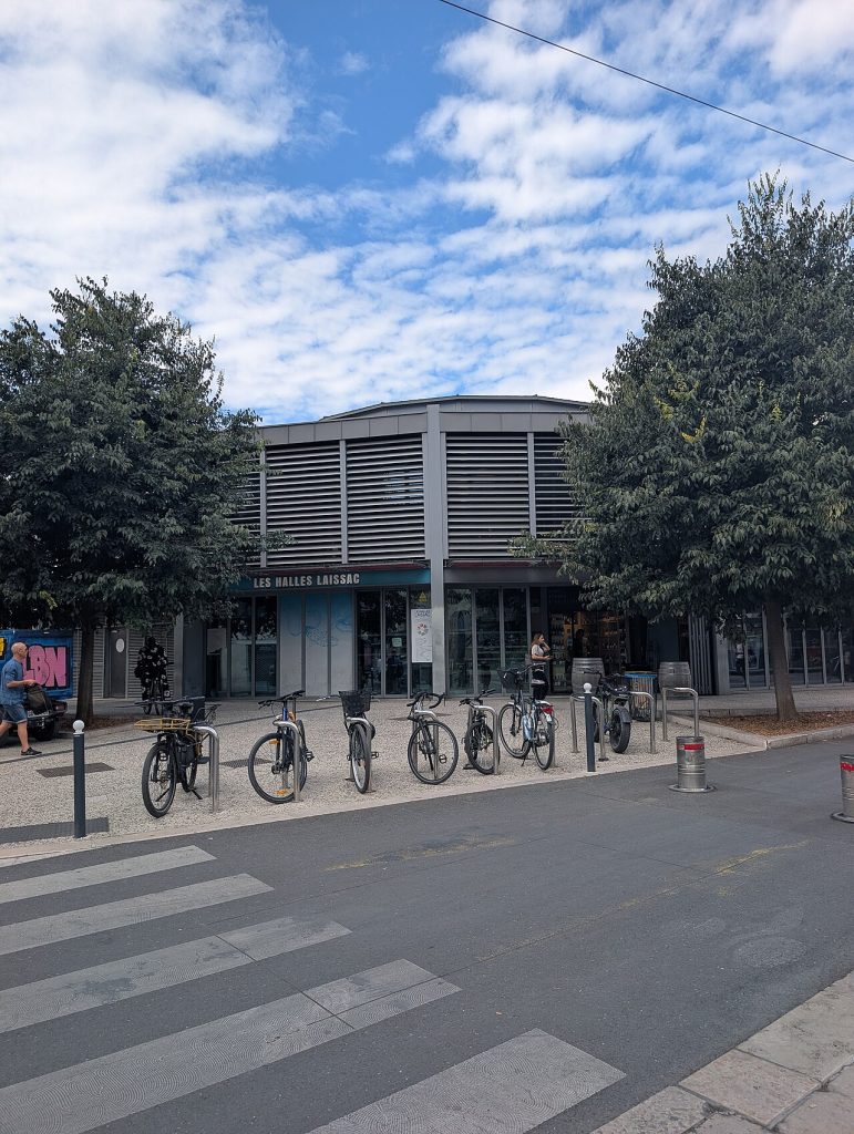 Façade des halles Laissac avec leur enseigne, des vélos garés devant et un passage piéton au premier plan