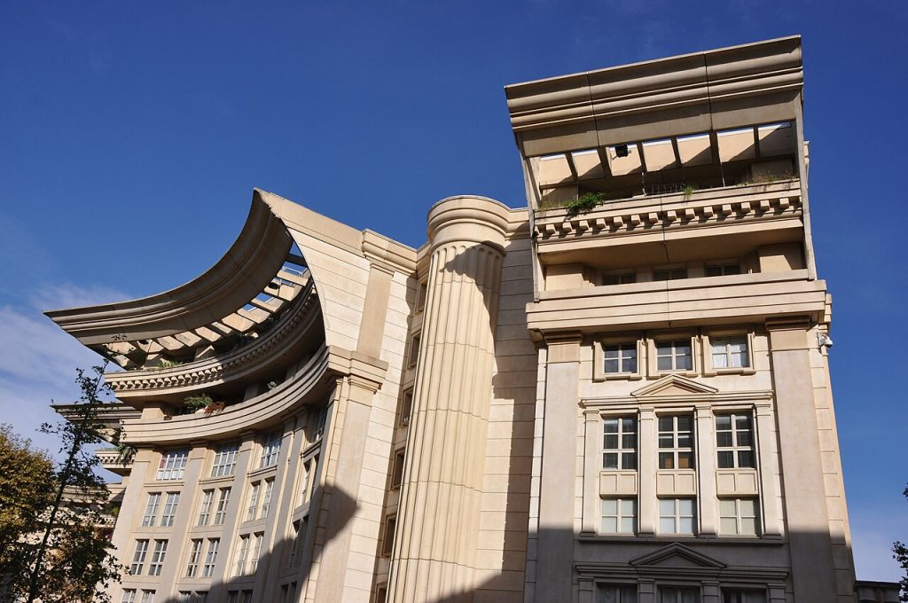 Immeubles d’Antigone avec une colonne géante et des corniches incurvées en surplomb, sous un ciel bleu