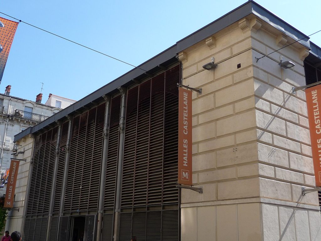 La façade des halles Castellane, avec ses hautes persiennes brunes et ses bannières orange au nom des halles