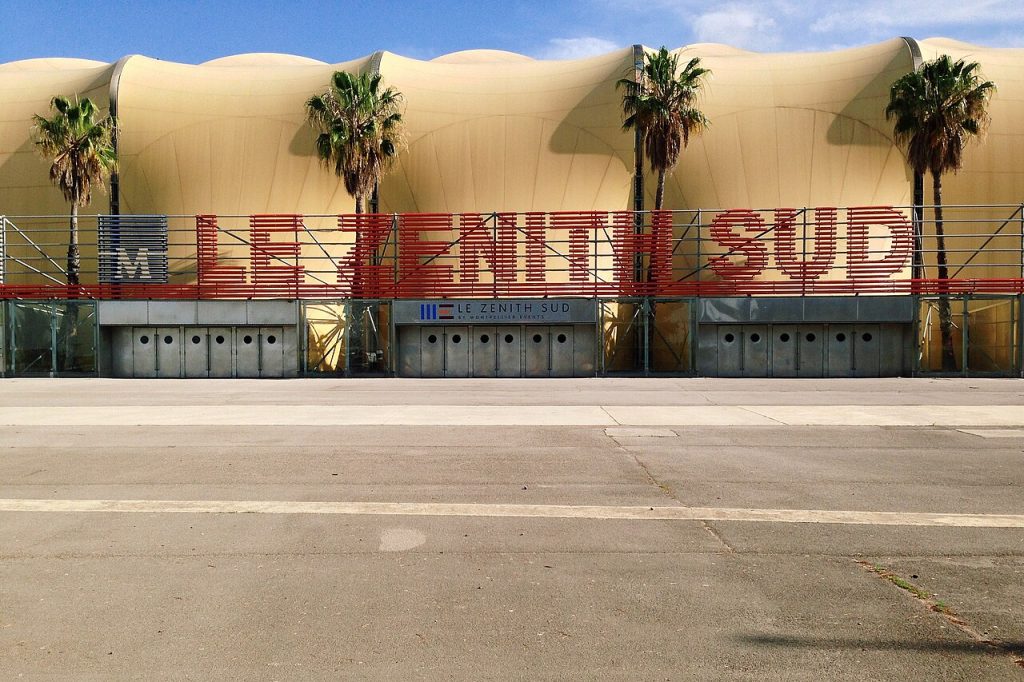 La façade du Zénith Sud, grande tente beige bordée de palmiers, avec son nom en lettres rouges