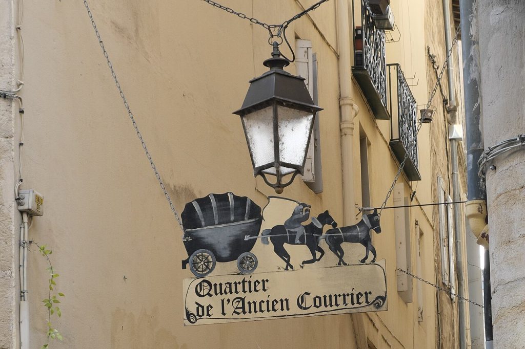 Enseigne en fer forgé « Quartier de l’Ancien Courrier » et lanterne, sur une façade de pierre de l’Écusson