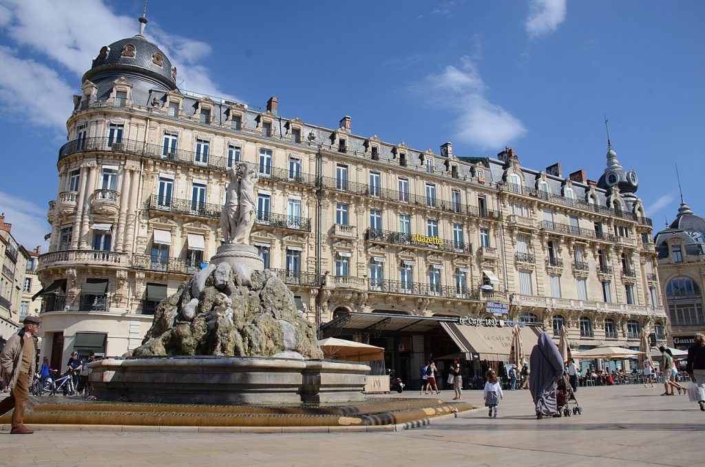 La fontaine des Trois Grâces devant les immeubles haussmanniens à dôme de la place de la Comédie, sous un ciel bleu