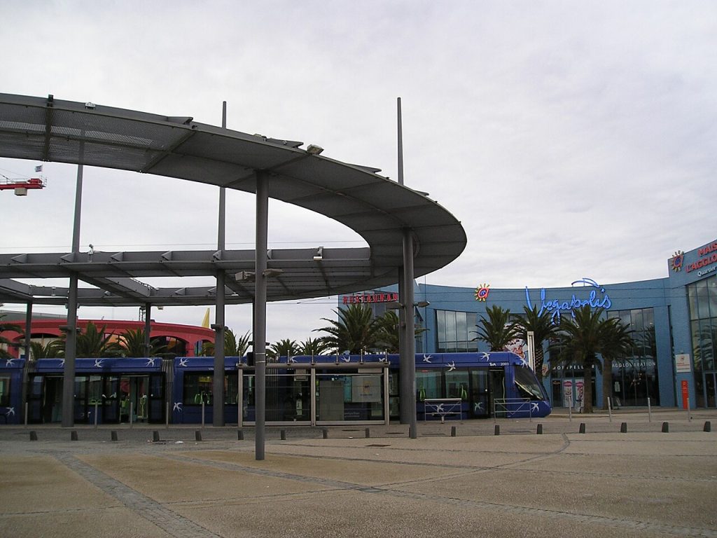 Un tram bleu de la ligne 1 à Odysseum, devant la patinoire Vegapolis et son enseigne lumineuse