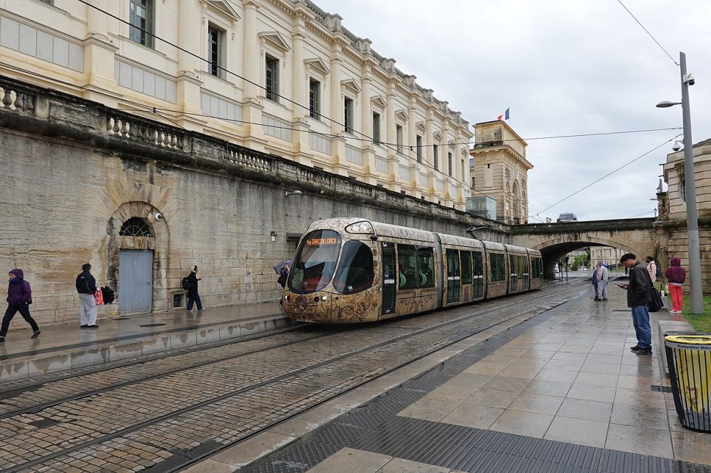 Un tram de la ligne 4 à la station Peyrou – Arc de Triomphe, longée d’un mur de pierre