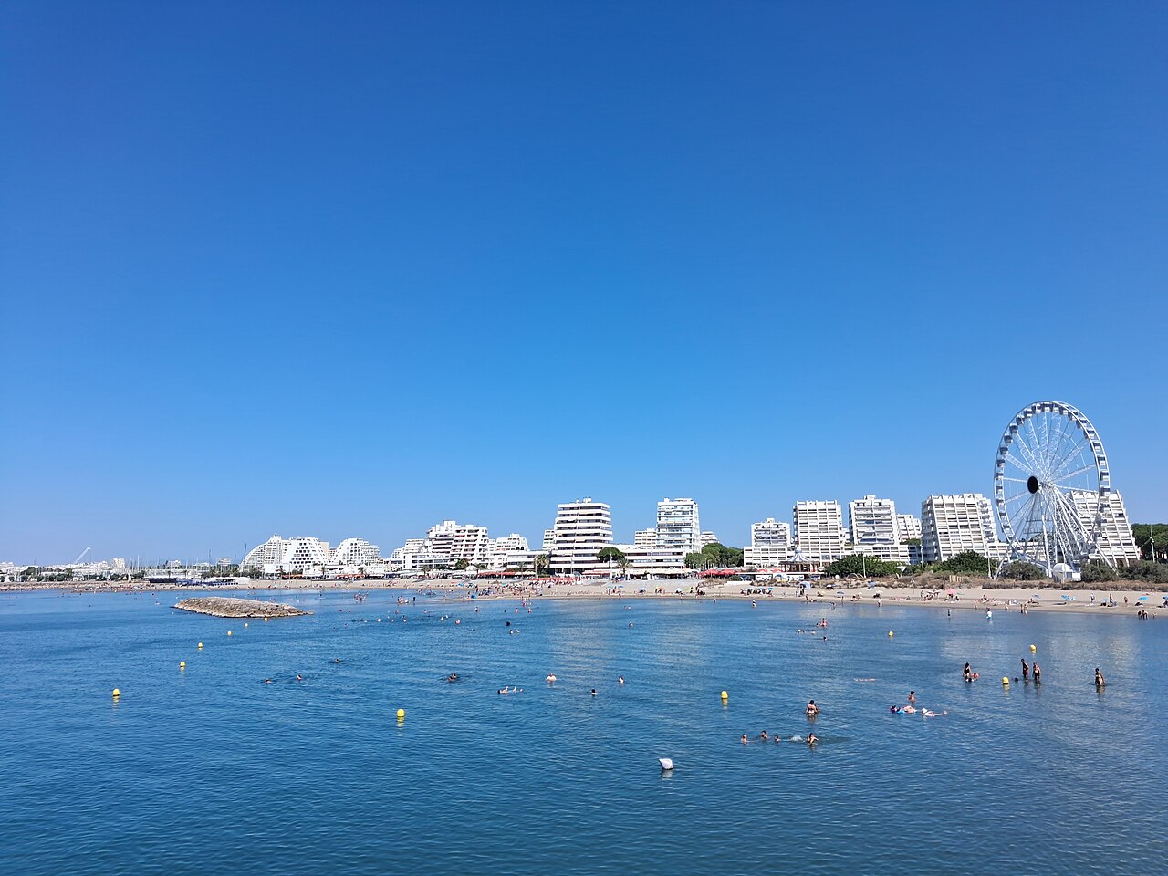 Baigneurs sur la plage de La Grande-Motte devant les immeubles pyramidaux et la grande roue